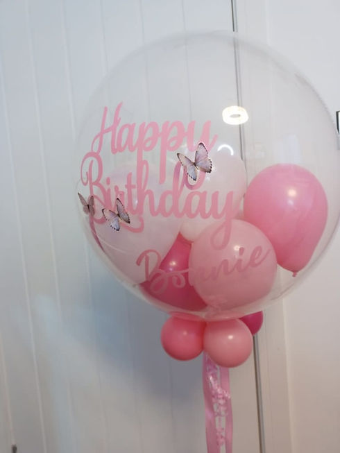 A large transparent bubble balloon with butterfly decorations, surrounded by pink balloons