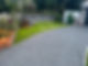 Landscaped area with gravel driveway, manicured green lawn, small brick planter, and fence border