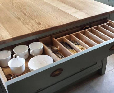Wooden cutlery drawer organiser inside a grey kitchen unit filled with cups