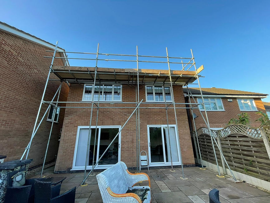 Two-story brick house with roofing under maintenance, covered by metal scaffolding on the upper half