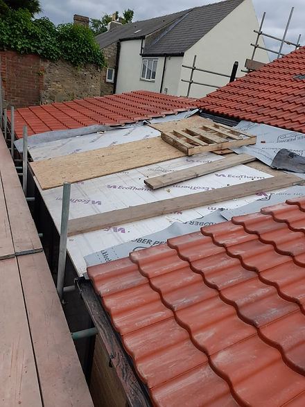 Partially constructed roof with red tiles, wooden planks, and underlayment materials