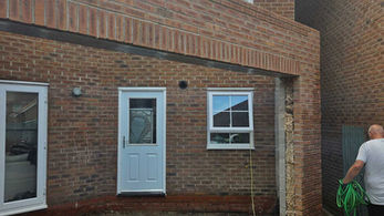 Man with green hose beside brick wall near white door and window