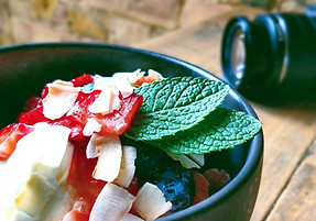 A bowl of fruit and yoghurt garnished with mint leaves