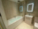 A bathroom with a glass shower enclosure, bathtub, and illuminated mirror on tiled walls