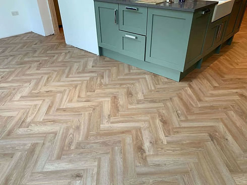 Elegant light oak herringbone flooring installed in a kitchen next to green cabinetry