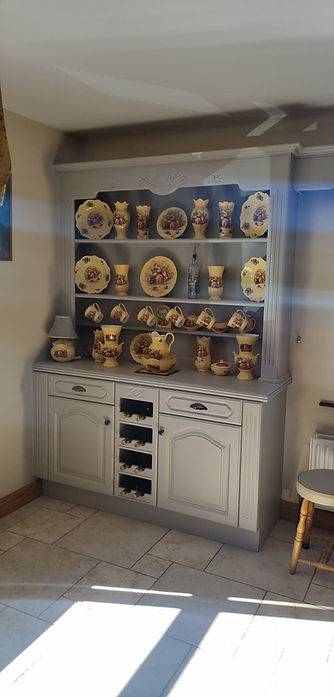 A grey hutch with decorative ceramic plates, jugs, and cups with floral designs
