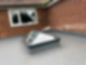 A modern skylight installed on a flat roof next to a brick wall