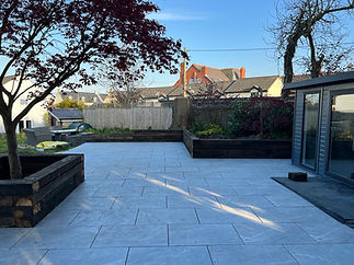 A spacious, newly paved patio surrounded by lush greenery in the back garden