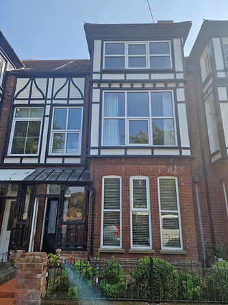 A terraced house facade with large windows framed by dark timber, red brick exterior, and a small garden