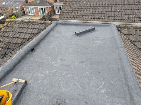 Newly installed smooth dark grey felt flat roof membrane on a residential building