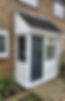 A small, enclosed porch with a dark grey door and white frame is attached to a brick house
