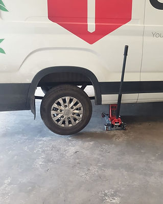 A hydraulic floor jack positioned under the rear wheel of a white van