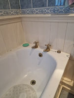 Interior corner of white acrylic bathtub with traditional chrome deck mounted pillar taps