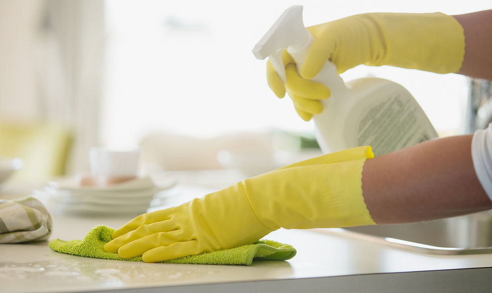 A woman in rubber gloves using a spray cleaner on a counter