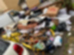 A large pile of discarded waste items stacked beside a white van in a cluttered area