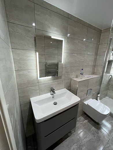 Modern bathroom with gray tiled walls, rectangular white basin vanity, Illuminated LED mirror, and wall-mounted toilet.