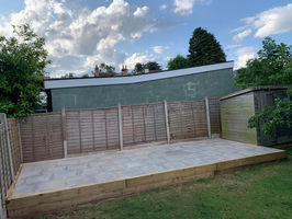 A newly paved patio area with wooden borders, surrounded by wooden fencing and greenery