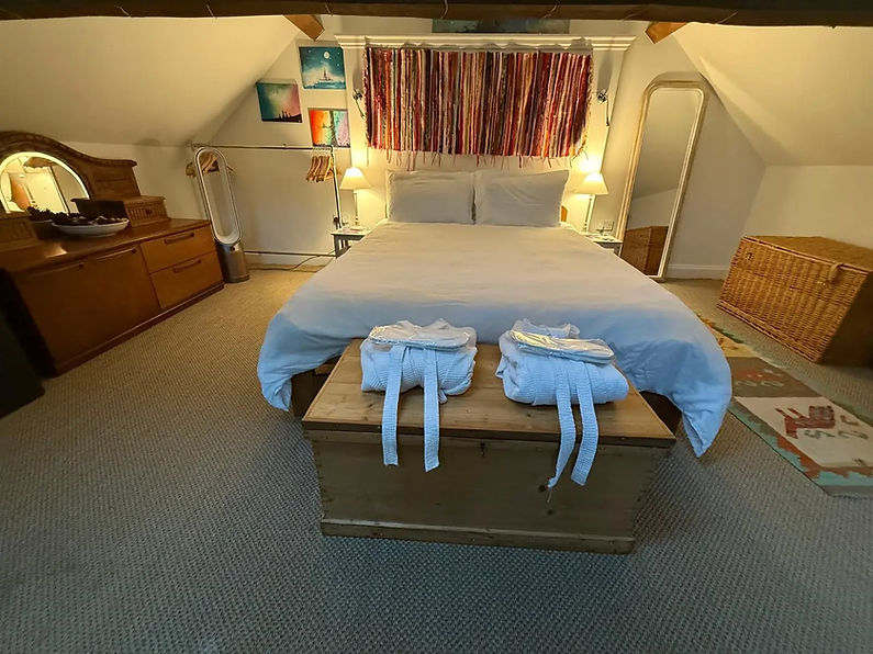 An attic bedroom with a neatly made bed, colourful wall decor, and soft lighting