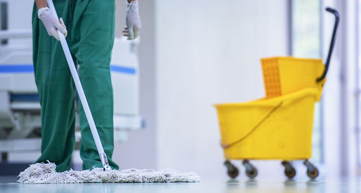 Person mopping a shiny, light-coloured floor in a clean environment, with a yellow mop bucket nearby
