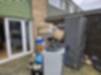A cluttered outdoor area filled with a fridge, boxes, a washing machine, and various items