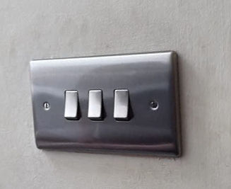 A metallic light switch panel with three toggles mounted on a textured wall