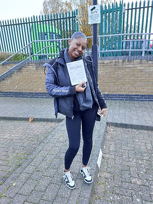 A woman in a black jacket stands on a pathway, holding a document