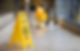 A yellow caution sign is placed on the tiled hallway floor, with a person mopping nearby