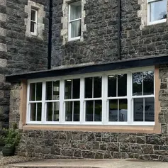 A stone house with large white-framed windows and a gravel path