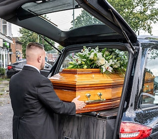 A pallbearer in a suit and tie, carefully handling a wooden coffin