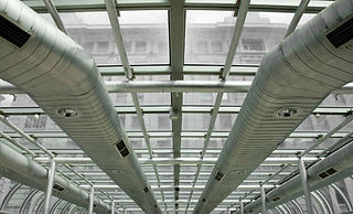 Ceiling view of a modern industrial interior with large silver ducts and a glass roof