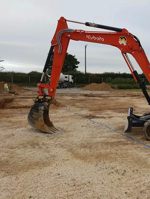 Red Kubota excavator arm and digger bucket operating on a site preparation area