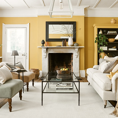 A living room with mustard yellow walls, a marble fireplace, and elegant furnishings