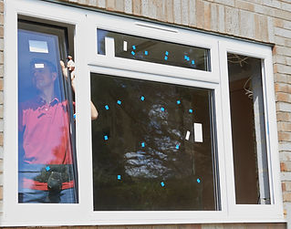 A person in a red shirt installs a large window on a brick building