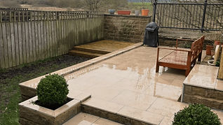 A patio with wet beige tiles, a wooden bench, and potted plants