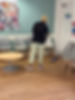 A person mopping the floor of a waiting room with grey chairs and a round wooden table