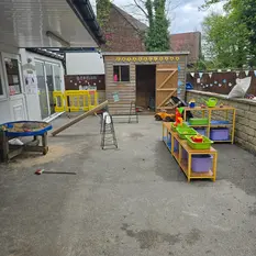 Outdoor playground area featuring a small wooden playhouse and plastic toy storage units