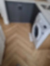 A room featuring a washing machine and herringbone-patterned wooden flooring