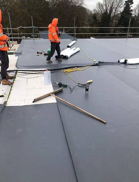 Roofers in safety wear working on a commercial flat roof membrane installation