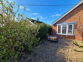 Brick house with a bay window on a sunny day, surrounded by lush greenery
