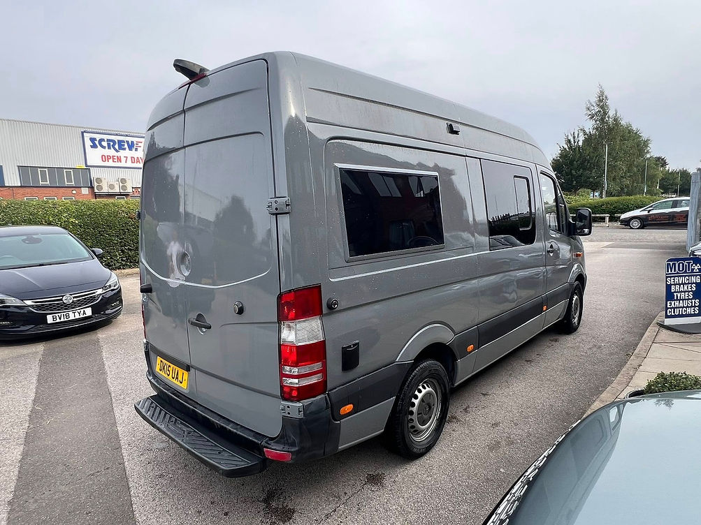 A grey van parked on a street near a hardware store, surrounded by other cars