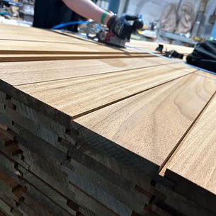 Smooth wooden boards stacked neatly, with a person in the background sanding one board