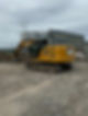 A yellow excavator works on a construction site, with industrial buildings in the background