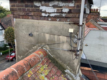 Worn chimney with moss-covered bricks and peeling paint sits atop a tiled roof