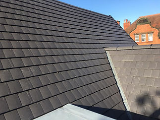 Dark grey tiled rooftop with a red brick building with tall chimneys
