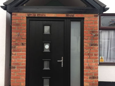 Modern black front door with glass panel and vertical windows, framed by red brick