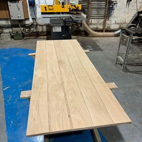 Wooden plank tabletop on a workshop floor with tools and machinery in the background