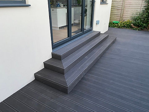 Modern grey composite deck with matching steps leads to glass patio doors of a house