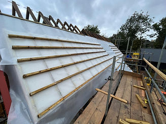 A partially constructed roof under construction with wooden slates being installed