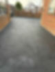 Freshly paved driveway with a smooth asphalt surface, bordered by brick walls