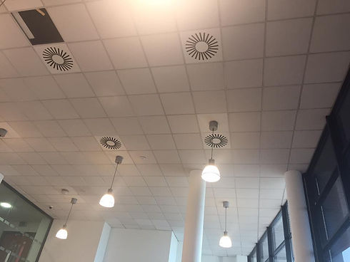Ceiling with white tiles, circular air vents, and hanging light fixtures in a modern interior